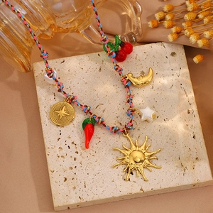 Détail d'un collier bohème en corde tressée avec breloques soleil, lune et cerise