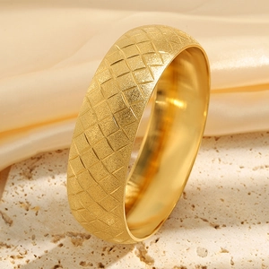 Macro detail of golden steel bracelet with matte rhombic texture on a beige stone base