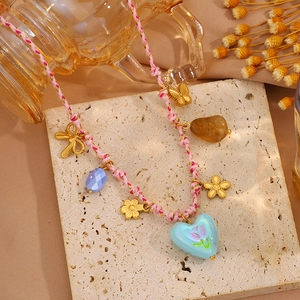 Détail du collier tressé rose avec breloques papillon dorées et pendentif cœur bleu