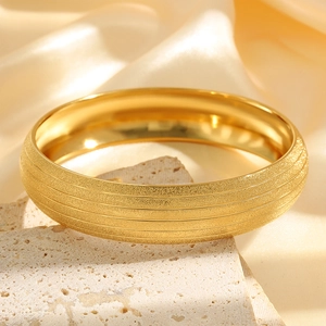 Detail of a matte gold titanium steel bangle with five horizontal stripes on travertine stone