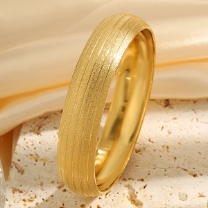 Detail of a matte gold-plated stainless steel cuff bracelet on beige textured stone