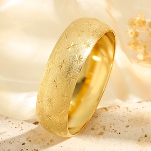 Close-up of golden titanium steel wide bangle with frosted finish and star engravings