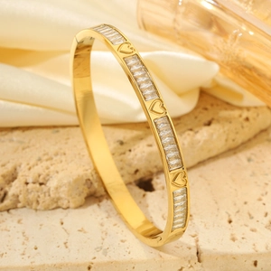 Detalle de la pulsera de trébol dorado con circonitas rectangulares sobre fondo de seda