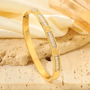 Primer plano de un brazalete de acero de titanio dorado con circonitas y motivos de tornillo