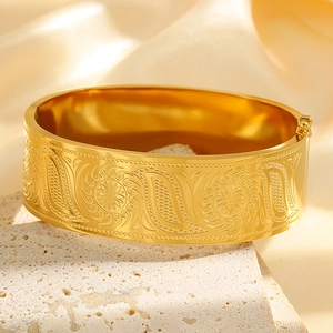 Detailed close-up of golden titanium steel bangle with floral engravings on silk background