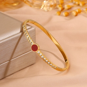 Detail of a gold titanium bangle with a central red gemstone and white zircon accents
