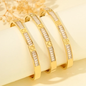 Detalle de pulseras de acero de titanio dorado con corazones trébol y circonitas