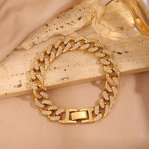 Detalle macro de pulsera de cadena cubana dorada con circonitas sobre seda y piedra