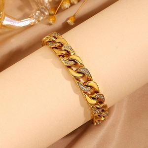 Detalle de pulsera de cadena cubana dorada con eslabones de circonita sobre fondo de satén