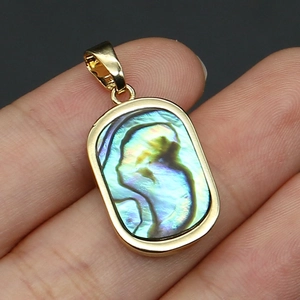 Macro shot of rectangular abalone shell pendant with gold plating held by a hand