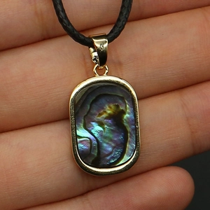Macro detail of rectangle shell pendant with gold rim and iridescent colorful abalone luster