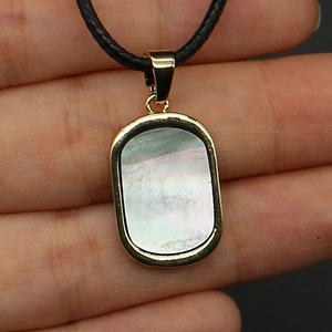 Close-up of rectangle shell pendant with gold edges held by hand showing size and detail