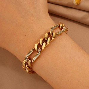 Lujosa pulsera de cadena cubana chapada en oro con brillantes pedrería sobre fondo de tela