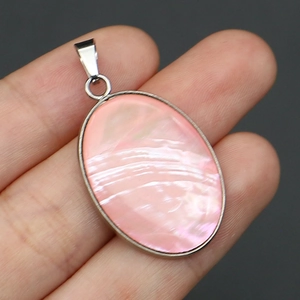 Detalle macro de un colgante ovalado con nácar rosa en un marco de metal plateado pulido
