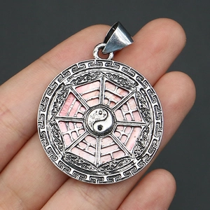 Close-up of a pink yin yang bagua pendant made of shell and alloy held by hand