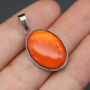 Vista macro de un colgante ovalado de concha naranja en la mano con cierre de metal plateado