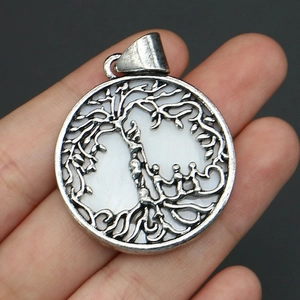 Close-up of a silver Tree of Life pendant with natural shell inlay held by hand