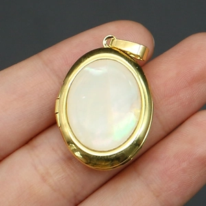 Detailed view of an oval locket pendant featuring natural white shell inlay in a gold finish