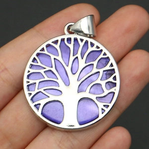 Macro shot of silver Tree of Life pendant with purple sea shell inlay held by hand