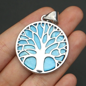 Detail view of a silver tree of life pendant with light blue shell inlay held by a hand