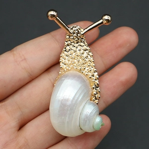 Detailed close-up of a golden snail brooch featuring a white shell and hammered metal texture