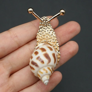 Macro shot of snail-shaped gold-plated brooch with natural shell and hammered metal texture