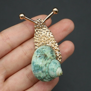 Detailed close-up of a gold snail brooch featuring a natural green spiral conch shell