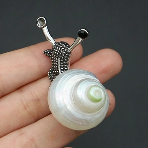 Détail d'une broche en forme d'escargot argenté avec une véritable coquille de nacre