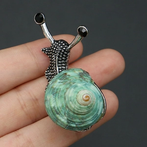 Détail d'une broche escargot en argent avec coquillage vert naturel et pierres noires