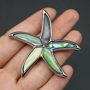 Macro detail of starfish brooch with colorful shell inlays held in hand for scale