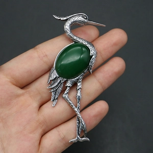 Macro shot of silver crane brooch with deep green stone and detailed feather textures