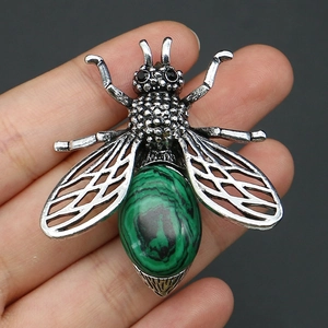 Détail macro d'une broche en forme d'abeille avec malachite, tenue à la main pour l'échelle