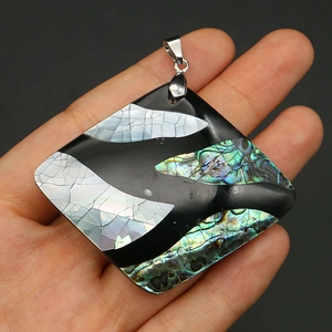 Close-up of a square pendant with natural abalone shell inlay held in hand for scale