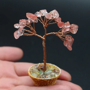 Miniature handmade rose quartz crystal tree shown on a fingertip for scale