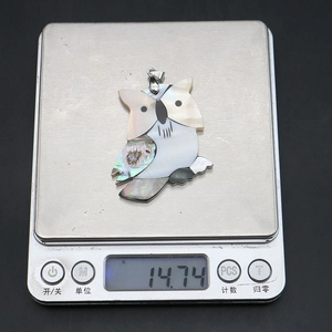 Détail du pendentif hibou en nacre affichant un poids de 14,74g sur une balance