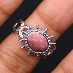 Detailed close-up of a pink stone ring with a sunburst frame and braided silver band