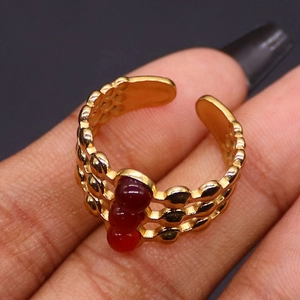 Makro-Detail von dreischichtigem Goldring mit drei roten Perlen und Wabenstruktur-Textur