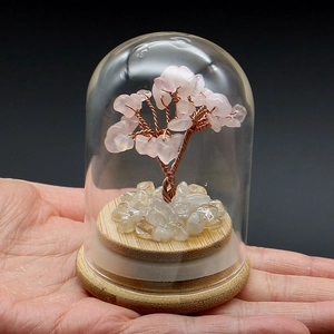 Detail of a pink crystal fortune tree in a glass dome with a natural wooden base