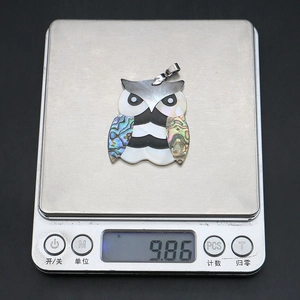 Vue détaillée du pendentif hibou en nacre sur une balance pesant 9,86 grammes