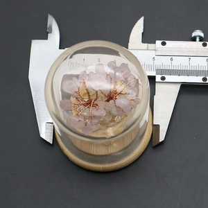Macro view of handmade pink crystal wish tree in glass dome with light wood base