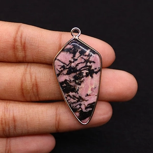 Detail of pink rhodonite stone pendant with gold plated edge held in hand