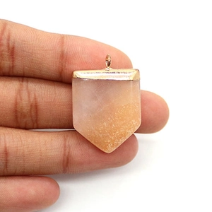 Détail macro du pendentif épée en pierre naturelle orange avec bélière dorée tenue à la main