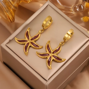 Détail de boucles d'oreilles étoile de mer dorées avec émail rouge sur fond en soie de luxe