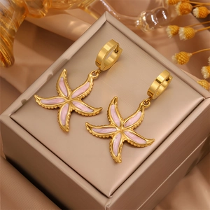 Détail de boucles d'oreilles étoile de mer dorées avec émail rose sur un coffret à bijoux