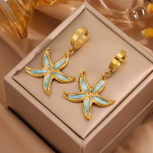 Vue macro de créoles étoile de mer dorées avec émail bleu clair sur boîte à bijoux