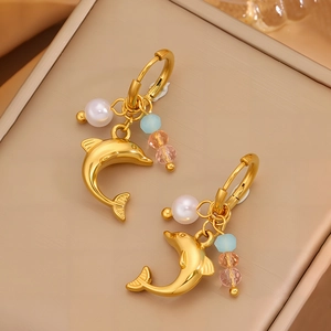 Goldene Delfin-Ohrringe mit Perlen und bunten Perlen auf beigem Schmuckkästchen-Hintergrund
