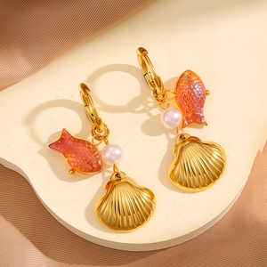 Detailaufnahme goldener Meeres-Ohrringe mit orangefarbenem Fisch, Perle und Muschel