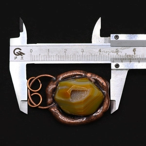 Macro view of 48mm natural agate pendant with copper wire wrap measured by caliper