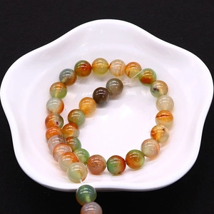 Polished natural agate stone beads in a white floral ceramic bowl on black background