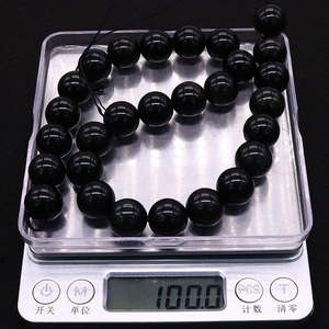 Nahaufnahme von natürlichen schwarzen Obsidianperlen auf einer Digitalwaage bei 100g